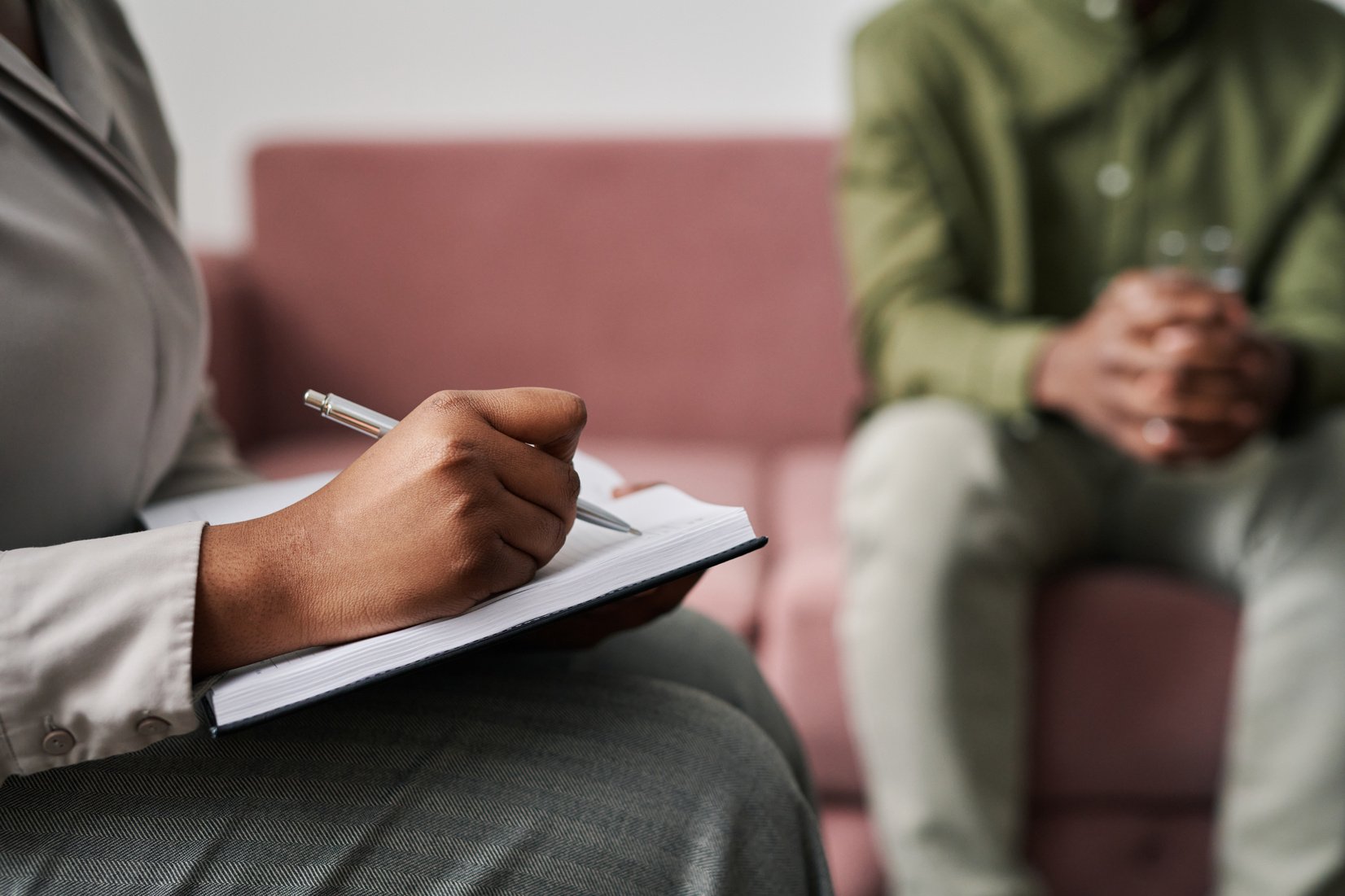 Hand of Young Female Psychoanalyst Making Notes in Notebook at Session